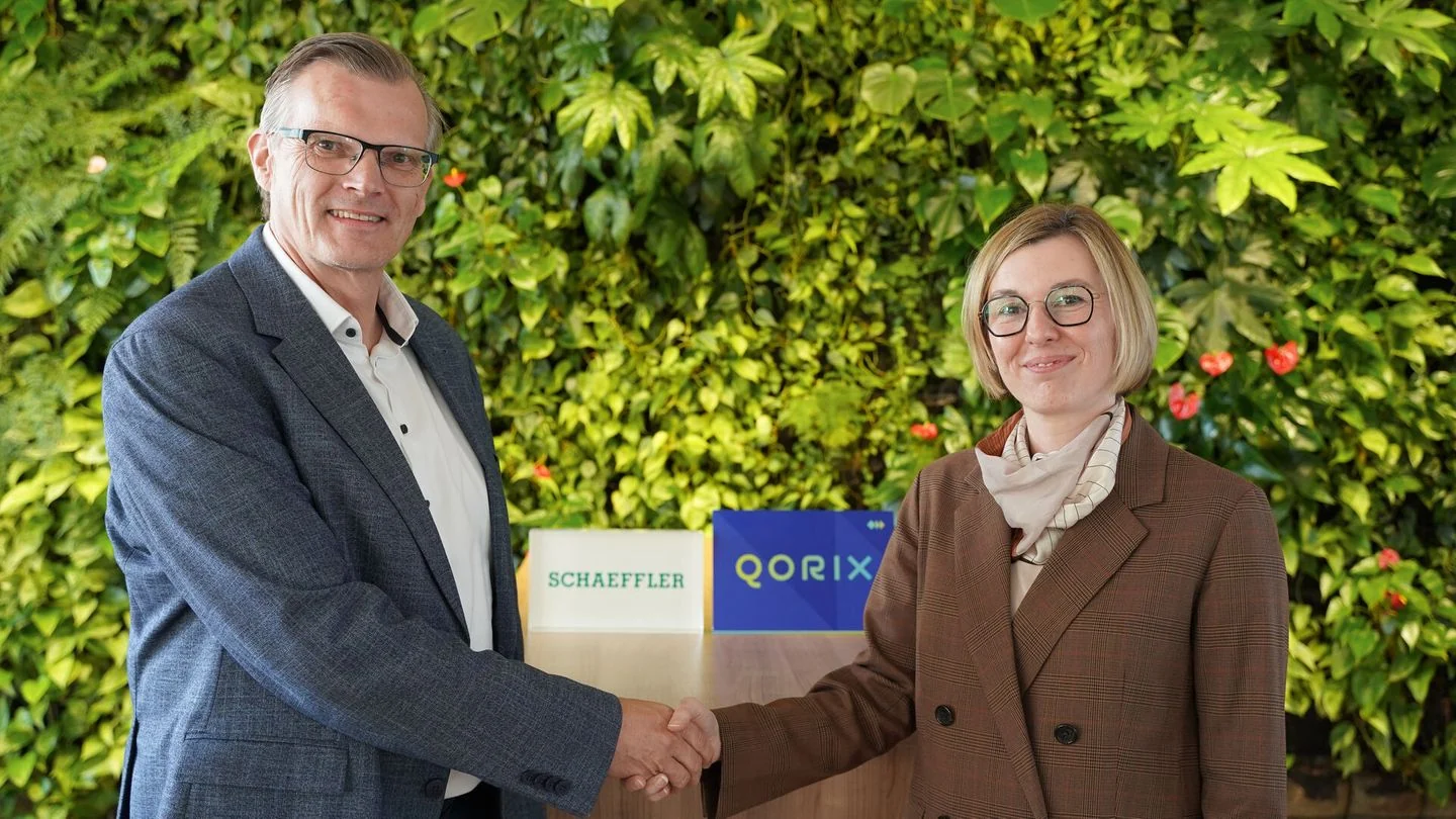 Gerd Winkler of Schaeffler and Caroline Pastjan of Qorix shaking hands in front of Schaeffler and Qorix signs.