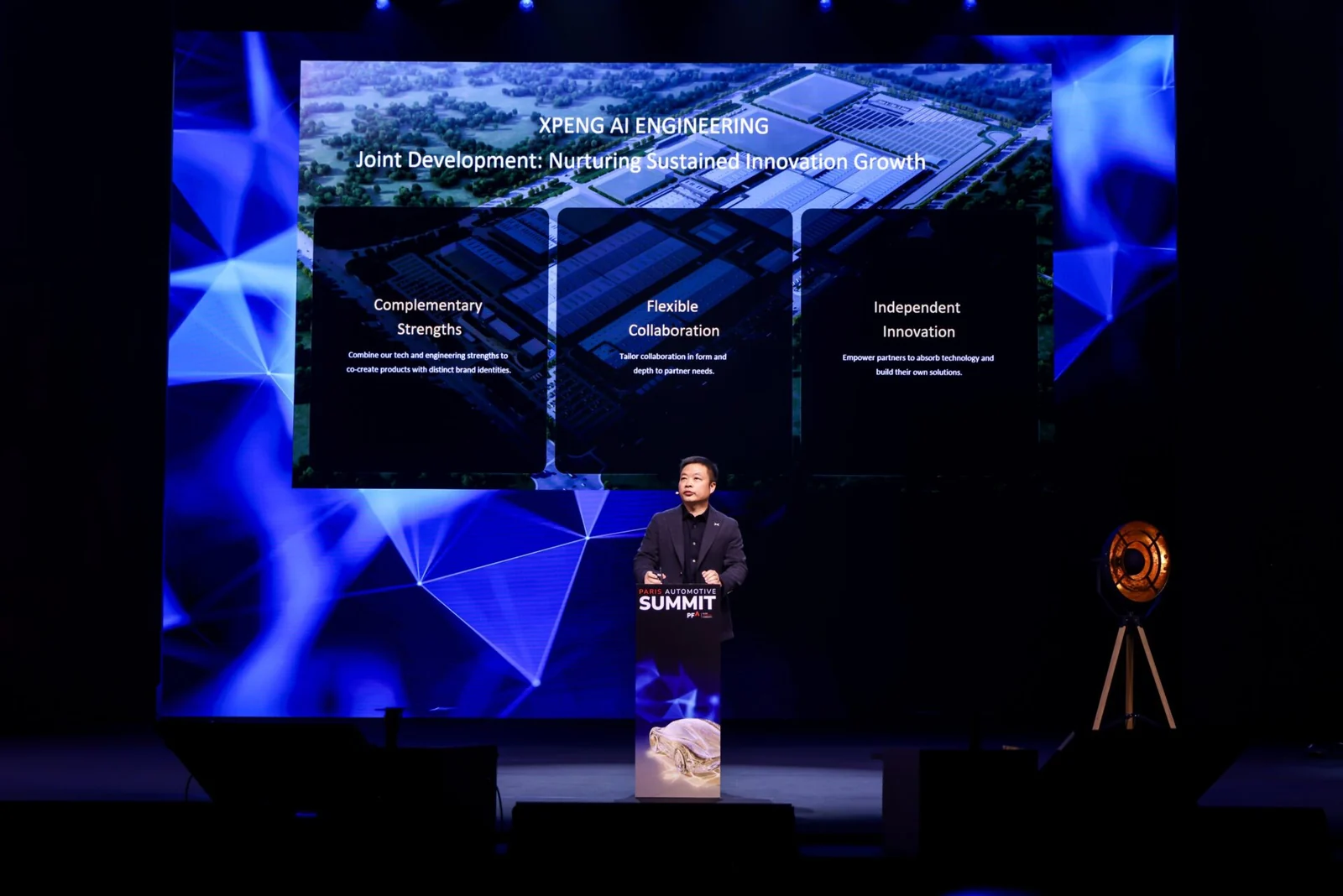 He Xiaopeng speaking at a lectern on stage, with an XPENG AI Engineering joint development slide displayed behind him.
